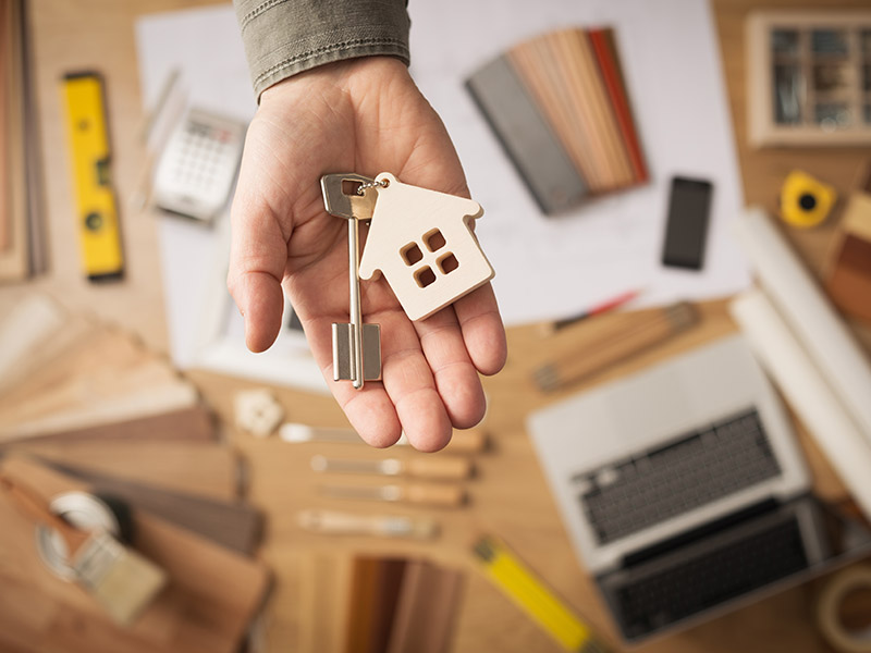 mão masculina segurando chave e miniatura de casa